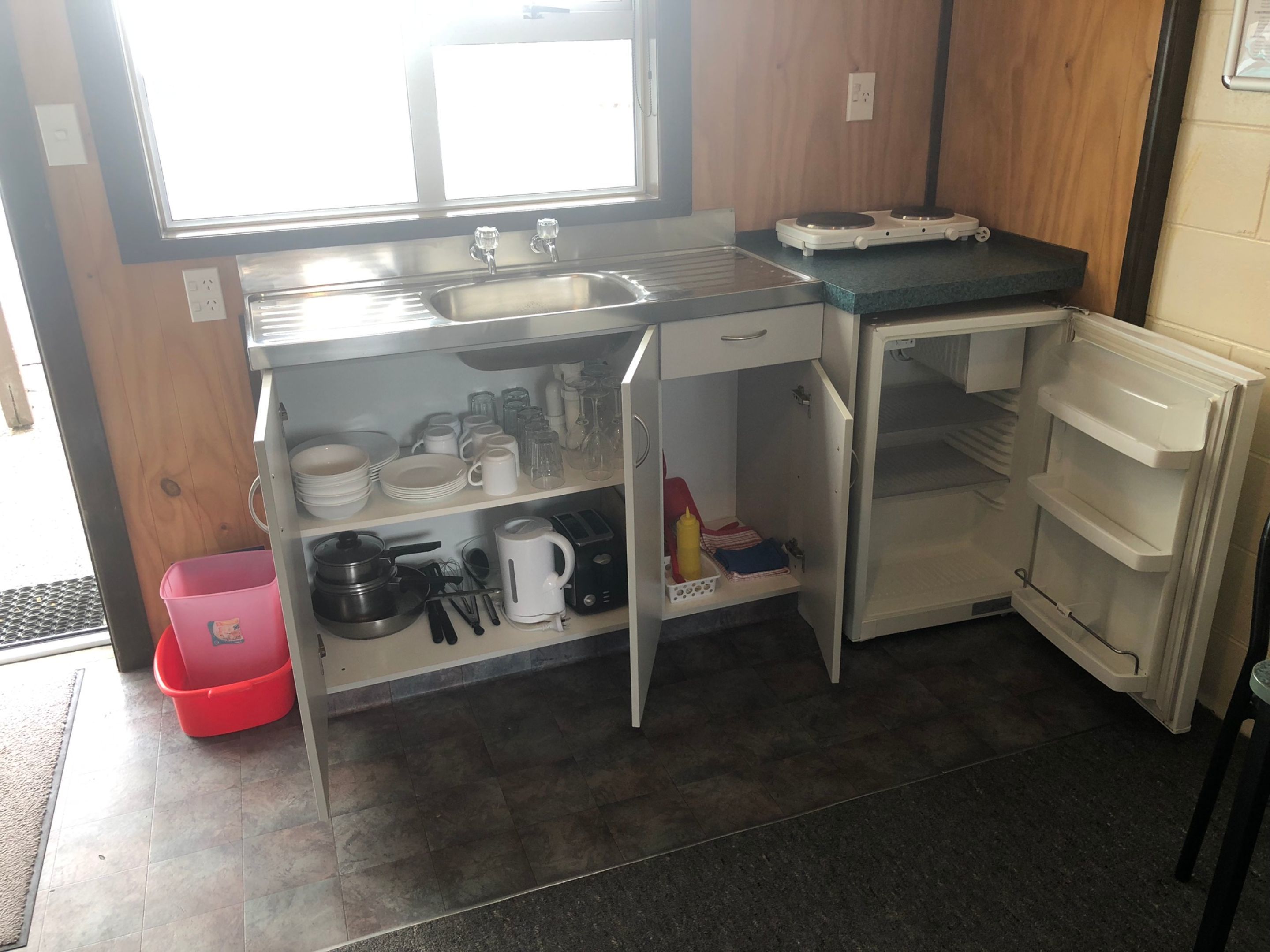 Una cocina compacta con un lavamanos, un refrigerador pequeño y repisas con vajilla y utensilios.