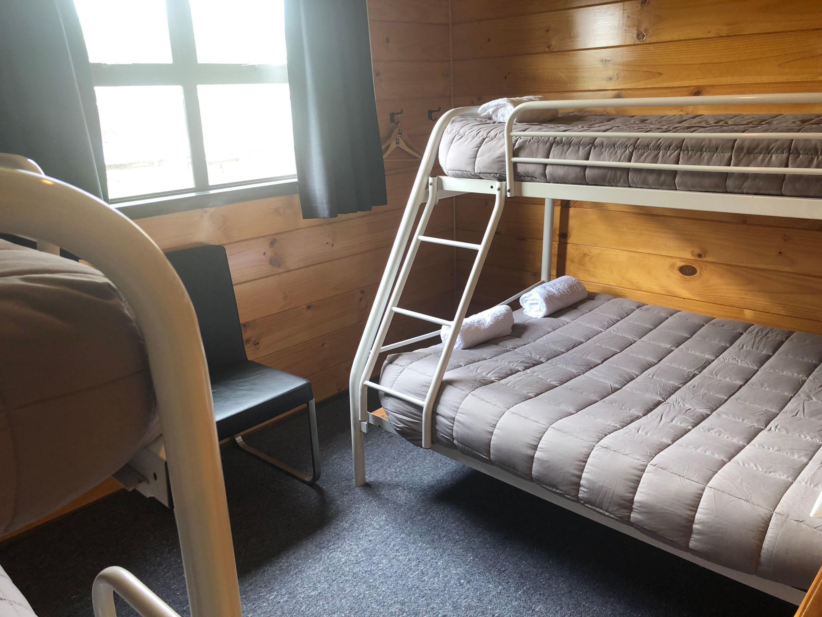 Un lit superposé avec une échelle, une chaise et une fenêtre avec des stores.