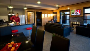 A modern kitchen with a person preparing food, a dining area with a table and chairs, a living room with a sofa and a TV, and a fireplace.