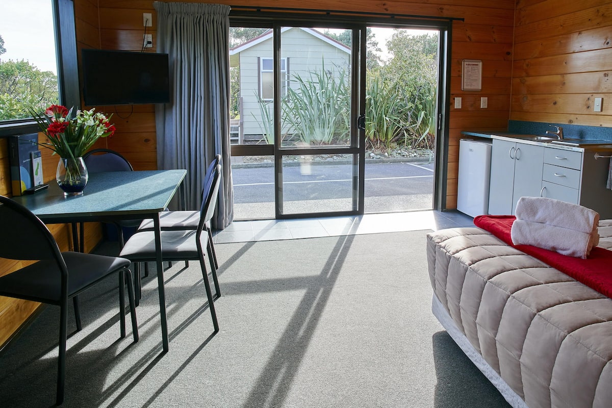 Ein Zimmer mit einem Bett, einem Tisch mit Stühlen, einem Fernseher und Blick ins Freie.