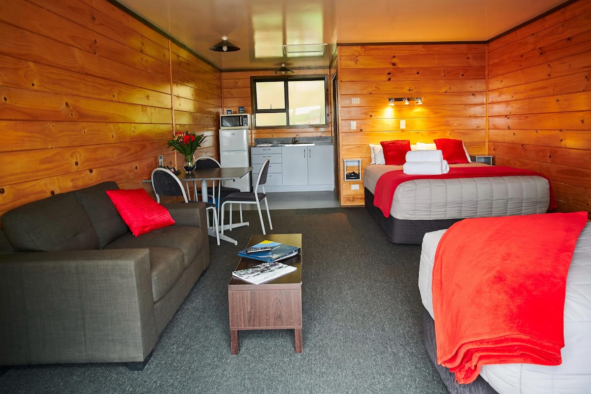 Ein gemütliches Zimmer mit einer Couch, zwei Betten, einem kleinen Tisch, einem Fernseher und einem Fenster.