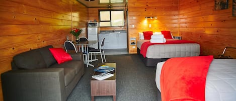 Una habitación acogedora con un sofá, dos camas, una mesita, un televisor y una ventana.