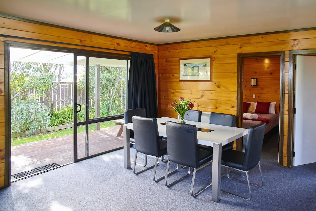 Eine Holzhütte mit Essbereich, einem Bett und Blick auf den Garten.