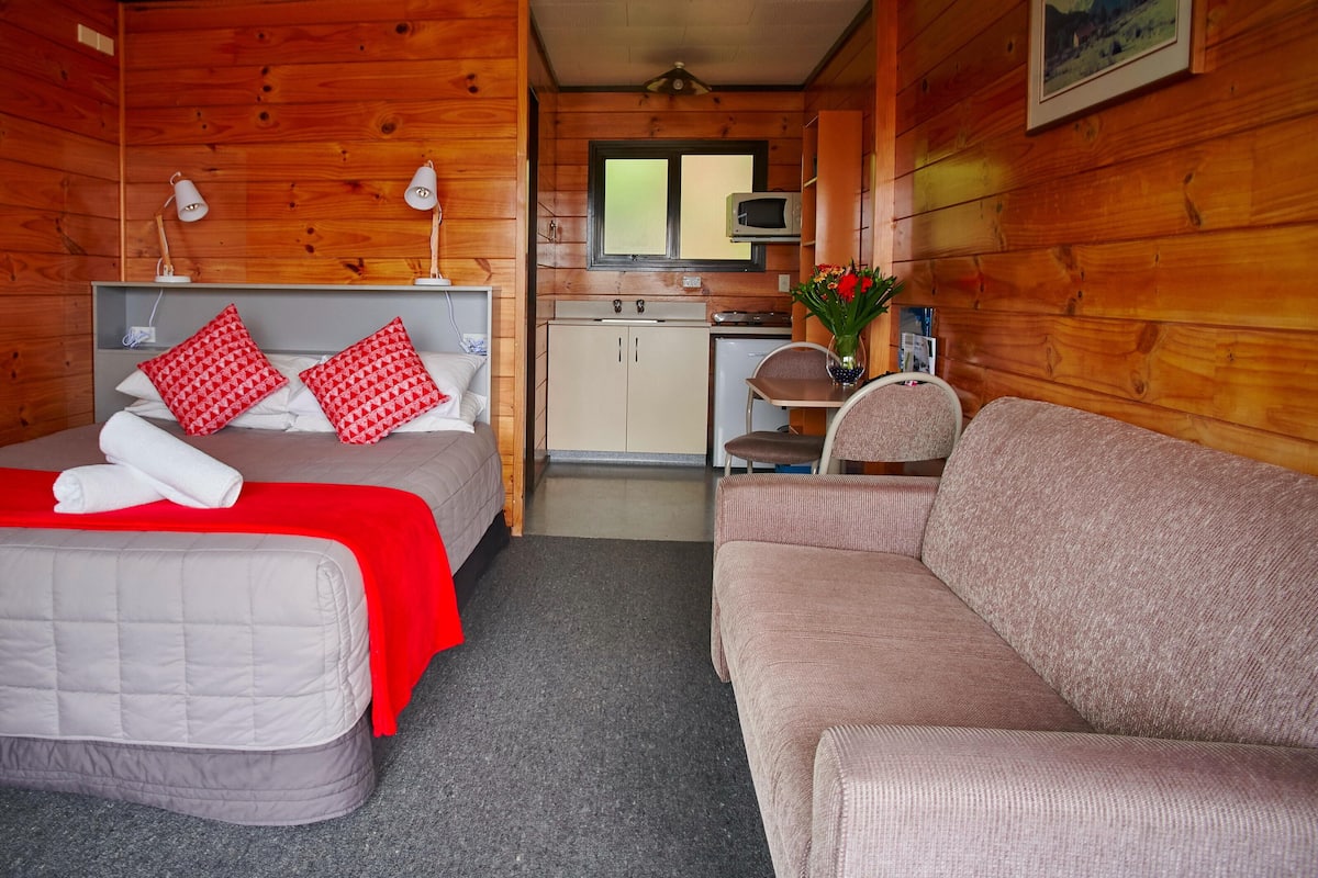 Ein gemütliches Blockhauszimmer mit Bett, Sofa, Küchenzeile und Essbereich.