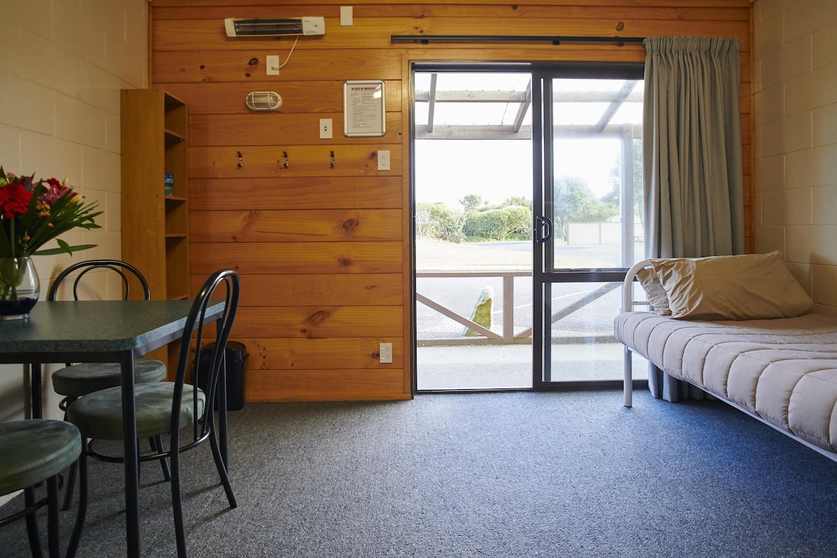Ein gemütliches Zimmer mit Holzvertäfelung, einem Esstisch mit Stühlen, einem Sofa und einer Glastür zum Außenbereich.