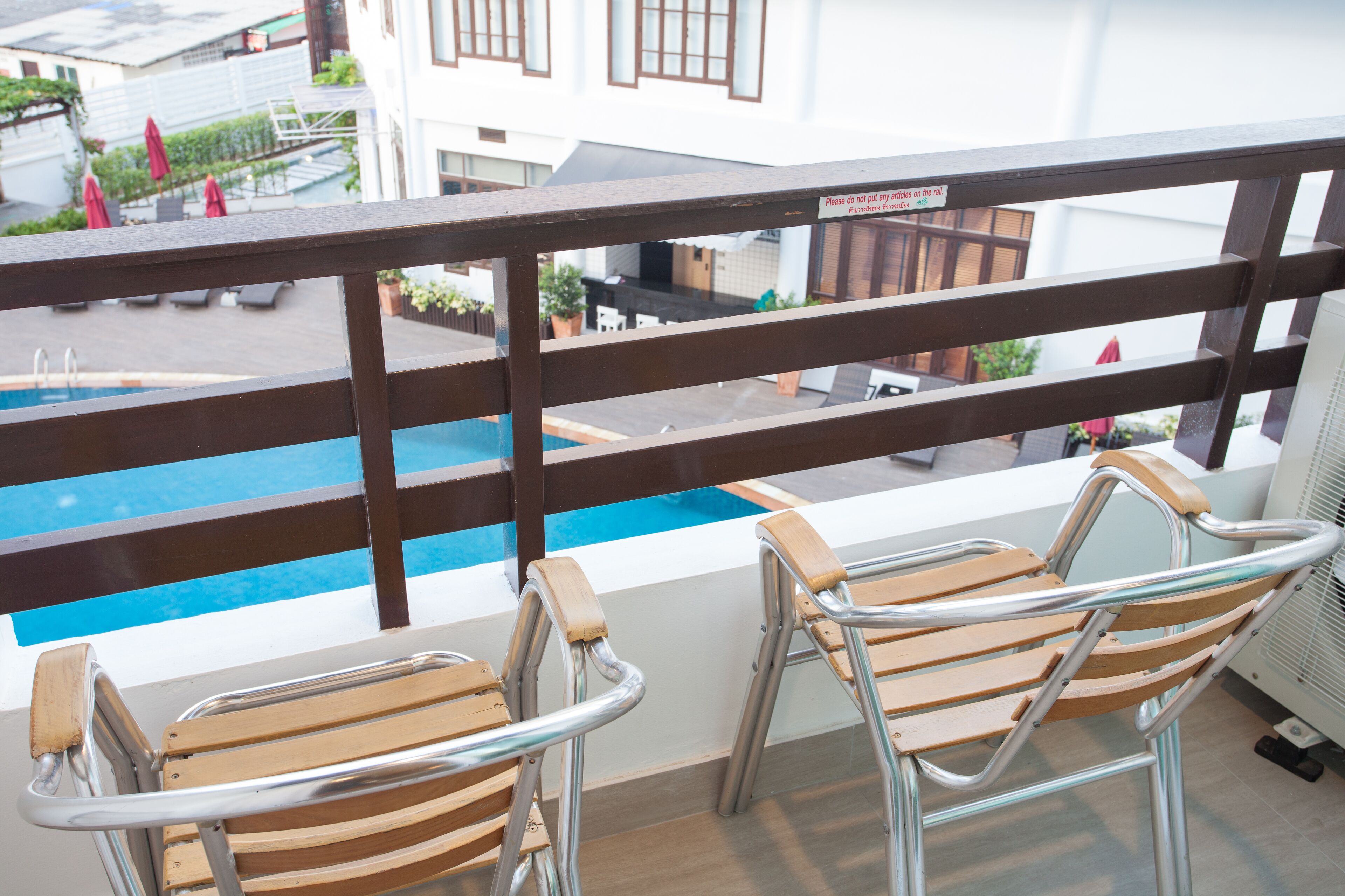 A balcony with a view of a swimming pool, two wooden chairs, and a railing.