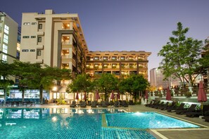 A hotel with a swimming pool, outdoor seating, and a well-lit facade.