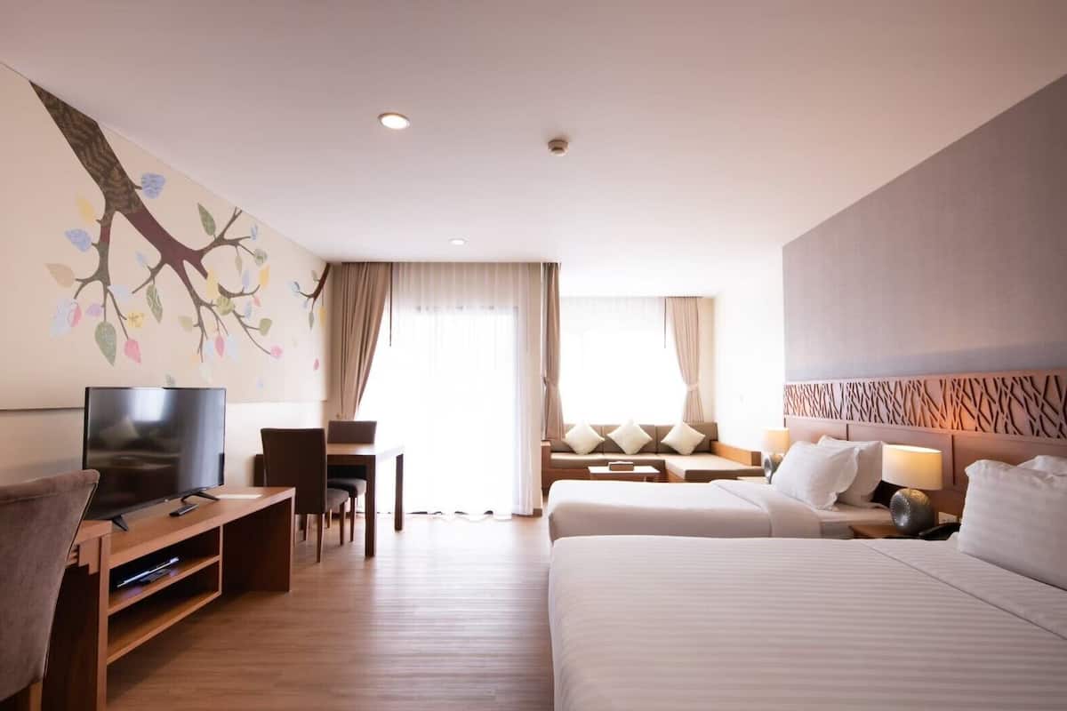 A hotel room with a bed, a TV, a desk, and a seating area with a view of the outdoors.