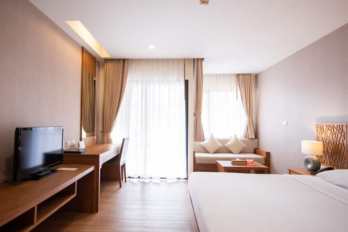 A hotel room with a bed, a desk with a TV, a sofa, and a lamp.