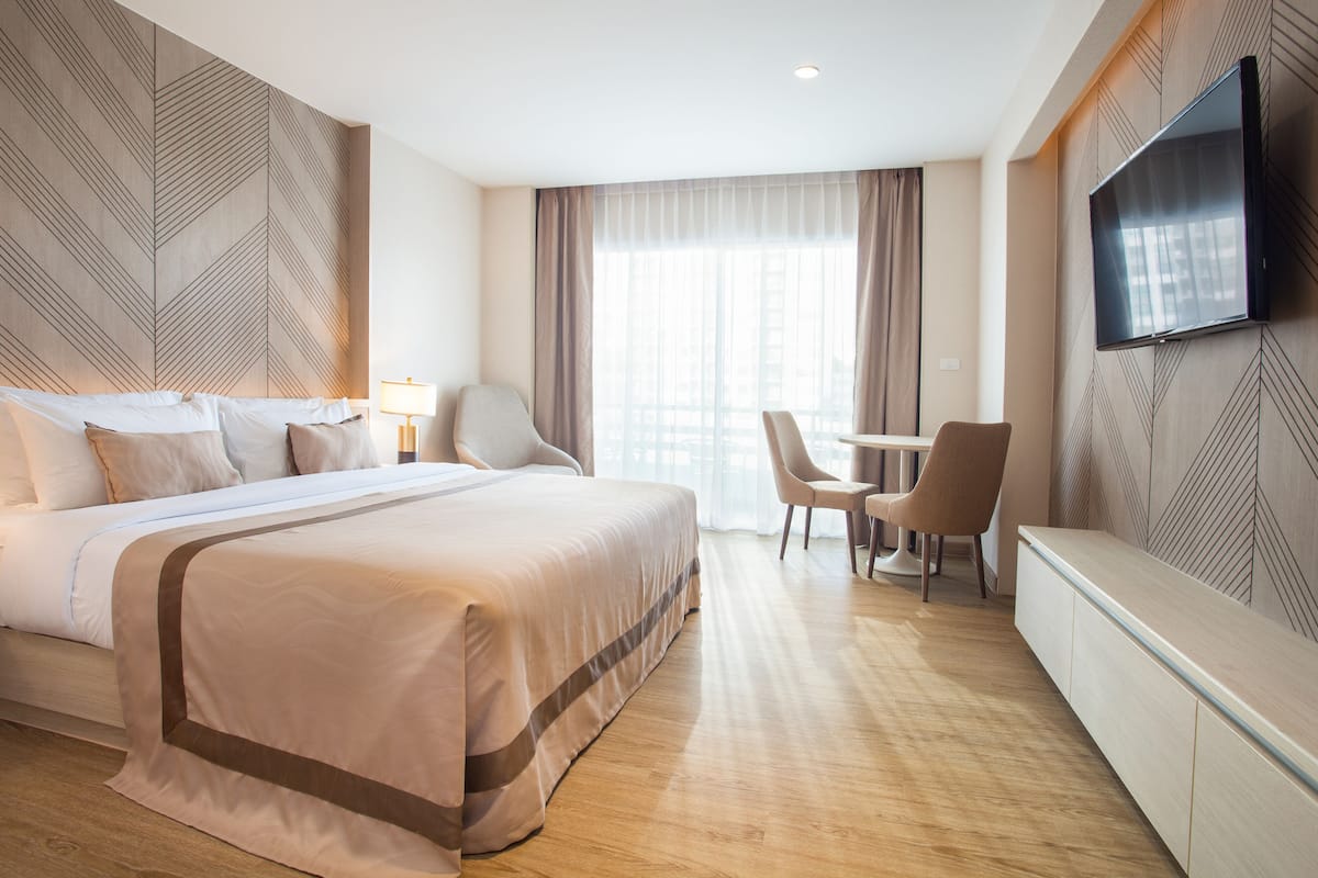 A hotel room with a large bed, a desk, a chair, and a TV mounted on the wall.