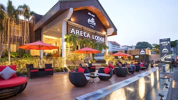 A hotel with outdoor seating, palm trees, and string lights.