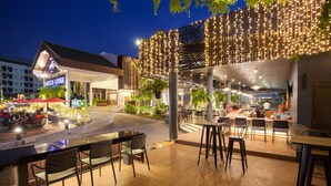 An outdoor dining area with tables and chairs, a covered seating area, and a building with a sign reading "ARECA LODGE". - Areca Lodge (Pattaya)