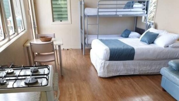 A compact room with a bunk bed, a small table with a bowl, and a gas stove. - Russell - Orongo Bay Holiday Park (Russell)