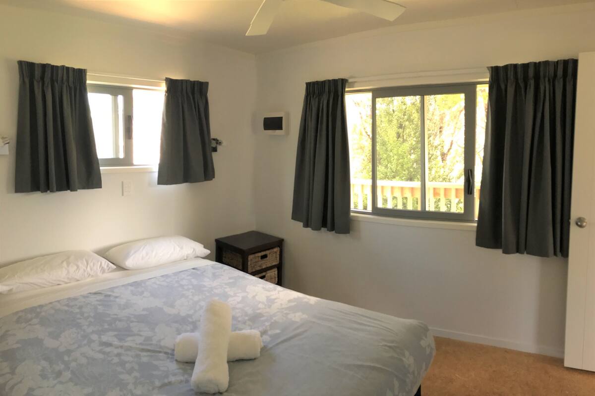 A bedroom with a bed, a nightstand, and a window with curtains.