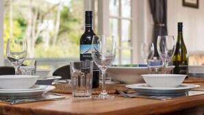 Una mesa de comedor dispuesta con copas de vino, una botella de Shingled y cuencos blancos sobre platos.