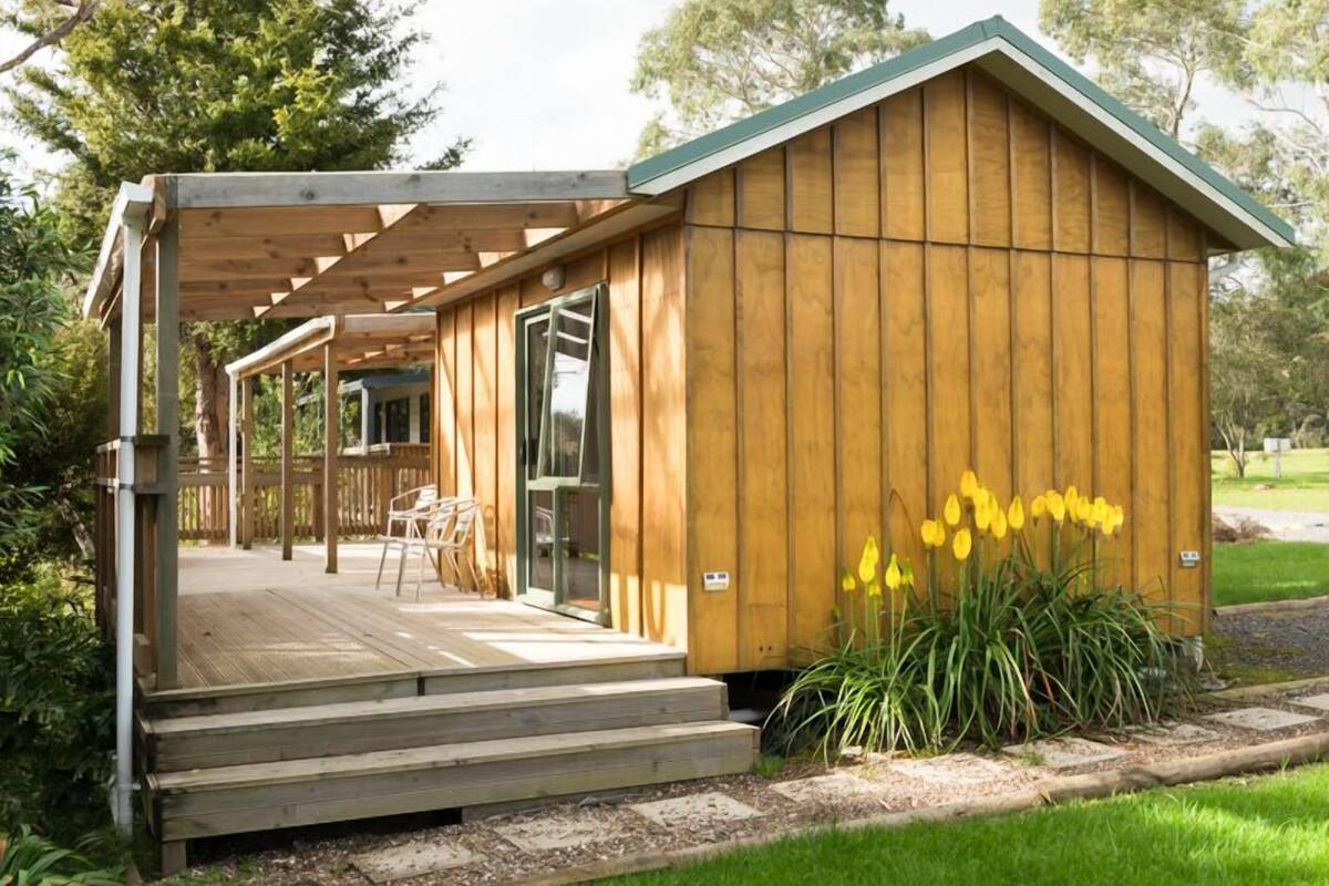 A wooden cabin with a porch, steps leading to the entrance, and a garden with yellow flowers.