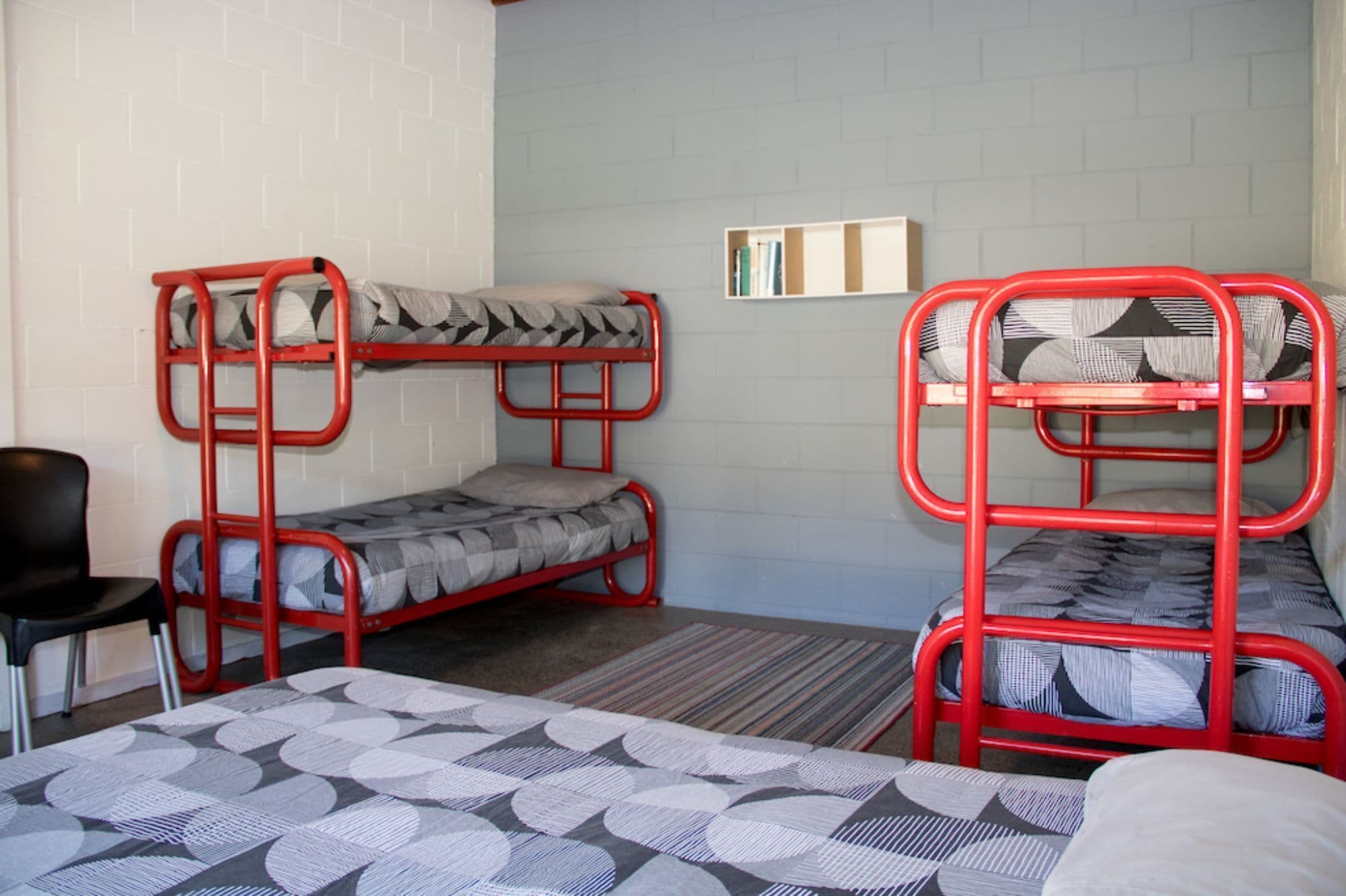A dormitory room with bunk beds, a desk, and a bookshelf.