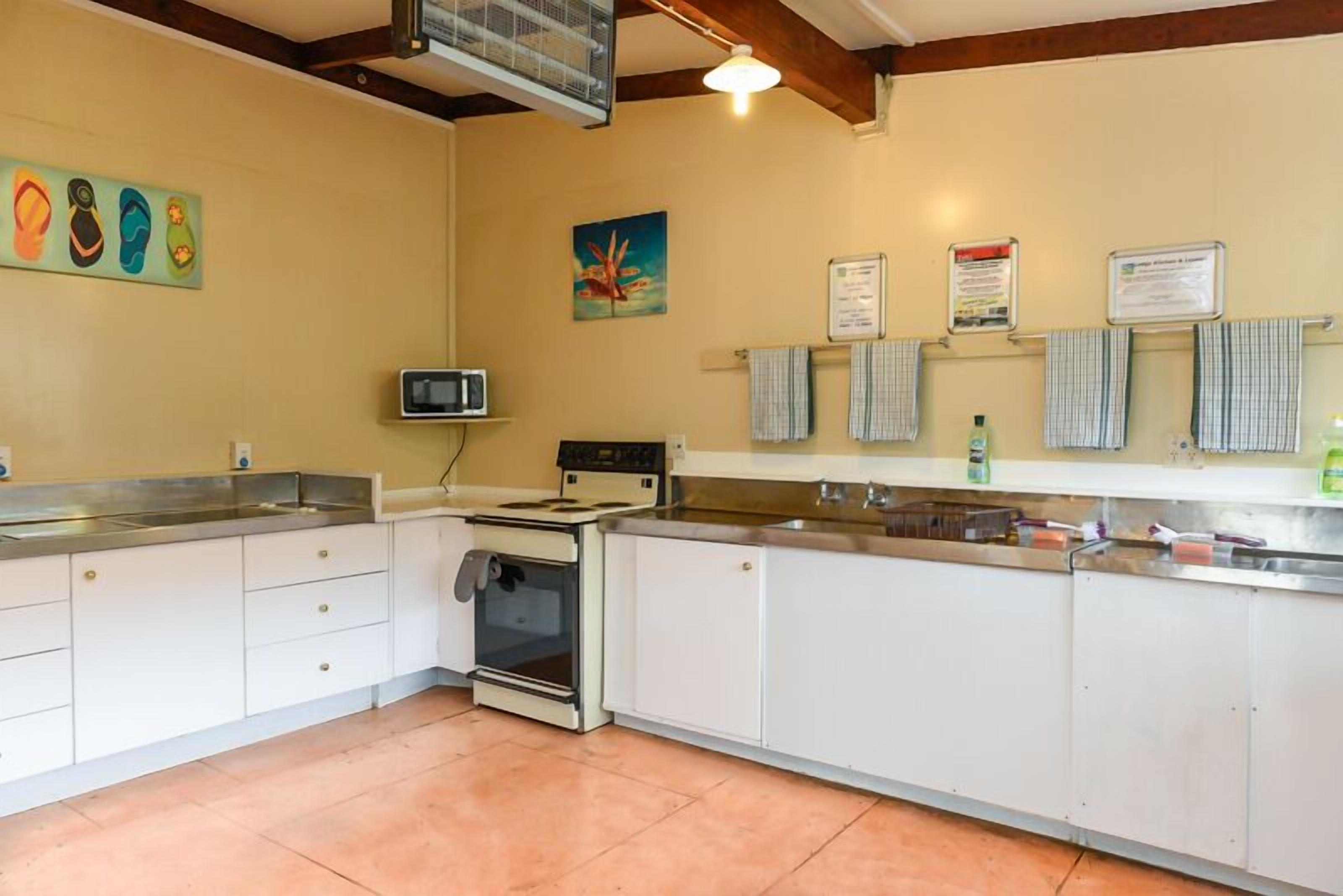Cocina con armarios blancos, estufa, microondas y lavamanos. Hay toallas colgadas en la pared y un cuadro sobre la estufa.