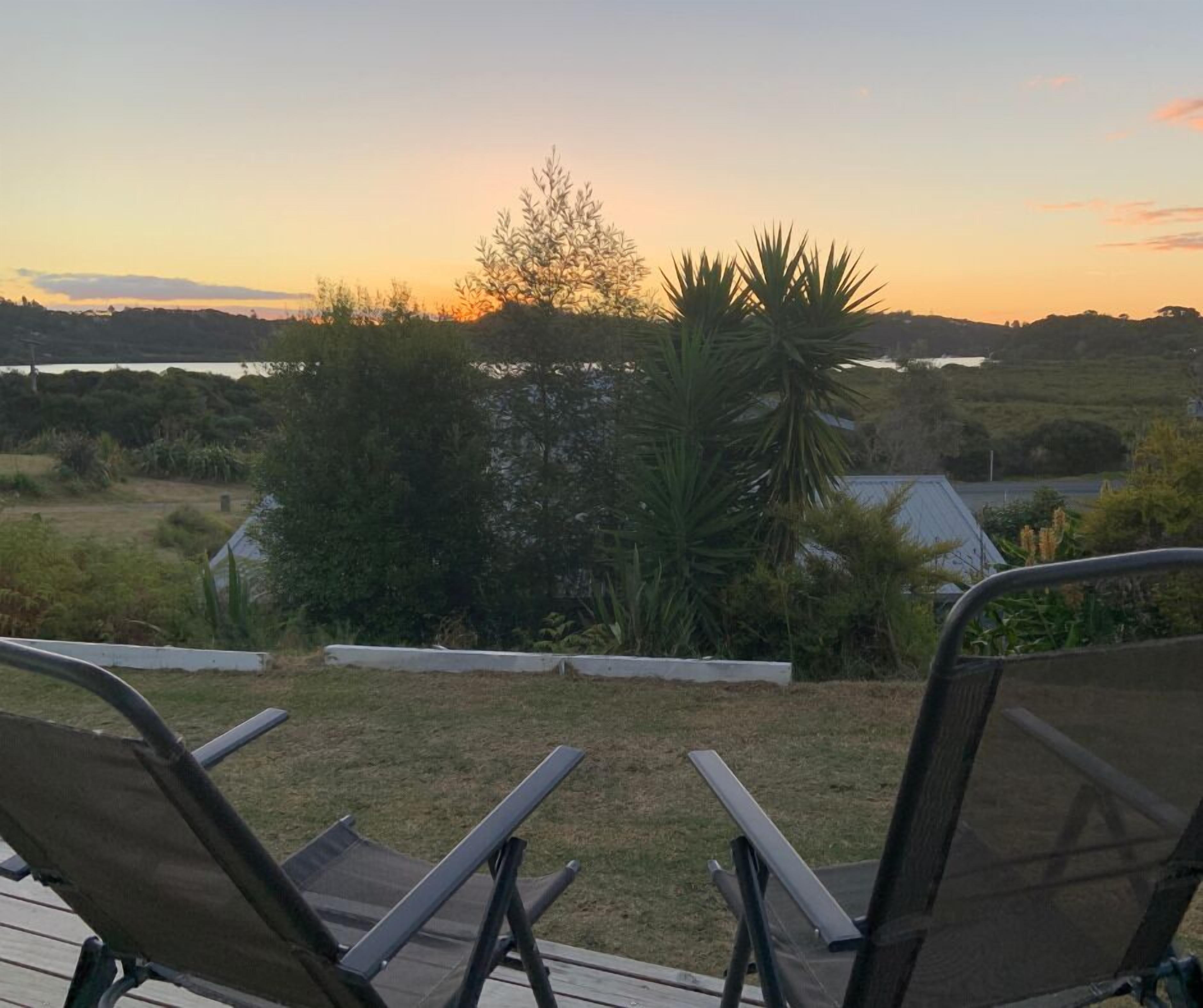 A deck with two lounge chairs overlooking a landscape with trees and a distant body of water during sunset.