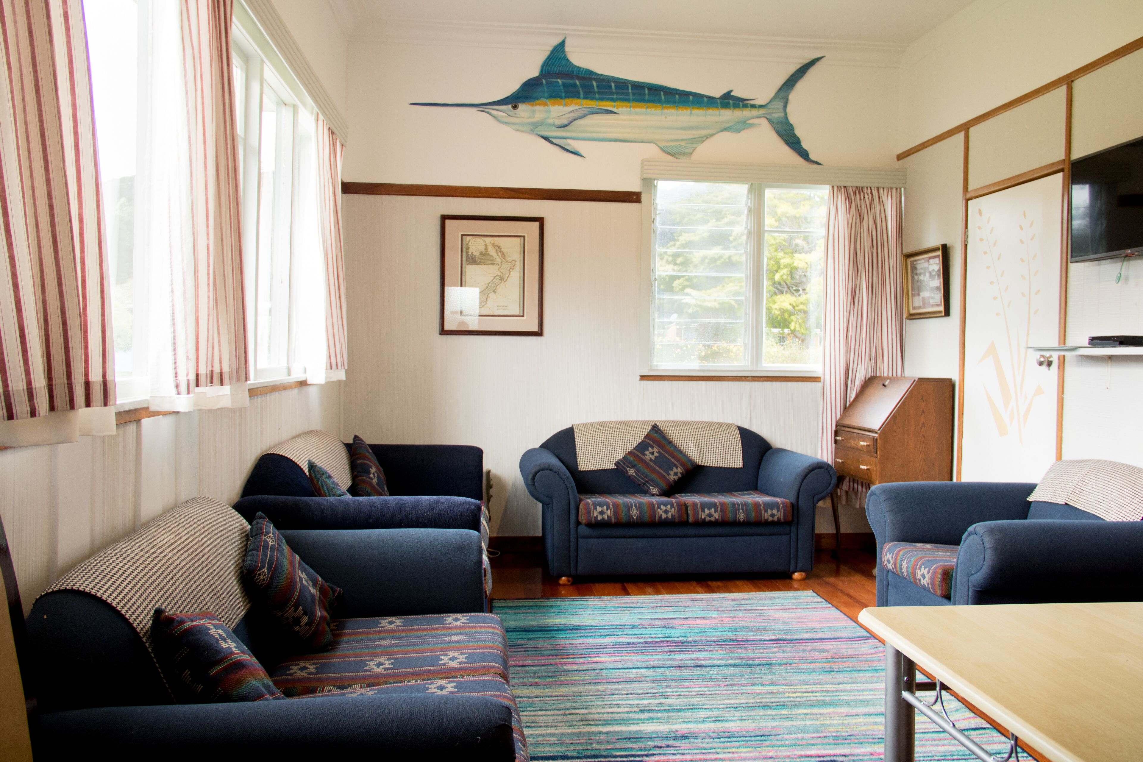Ein Wohnzimmer mit großem Fenster, einem blauen Sofa, einem Holztisch und einem an der Wand befestigten Fernseher.