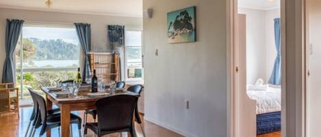 A dining area with a wooden table and chairs, a view of the outdoors, and a painting on the wall.