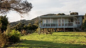 A house with a balcony, a picnic table, and a grassy yard. - Russell - Orongo Bay Holiday Park (Russell)