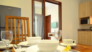 Un comedor con una mesa de madera dispuesta para dos personas, un televisor montado en la pared y una zona de cocina con armarios de madera.