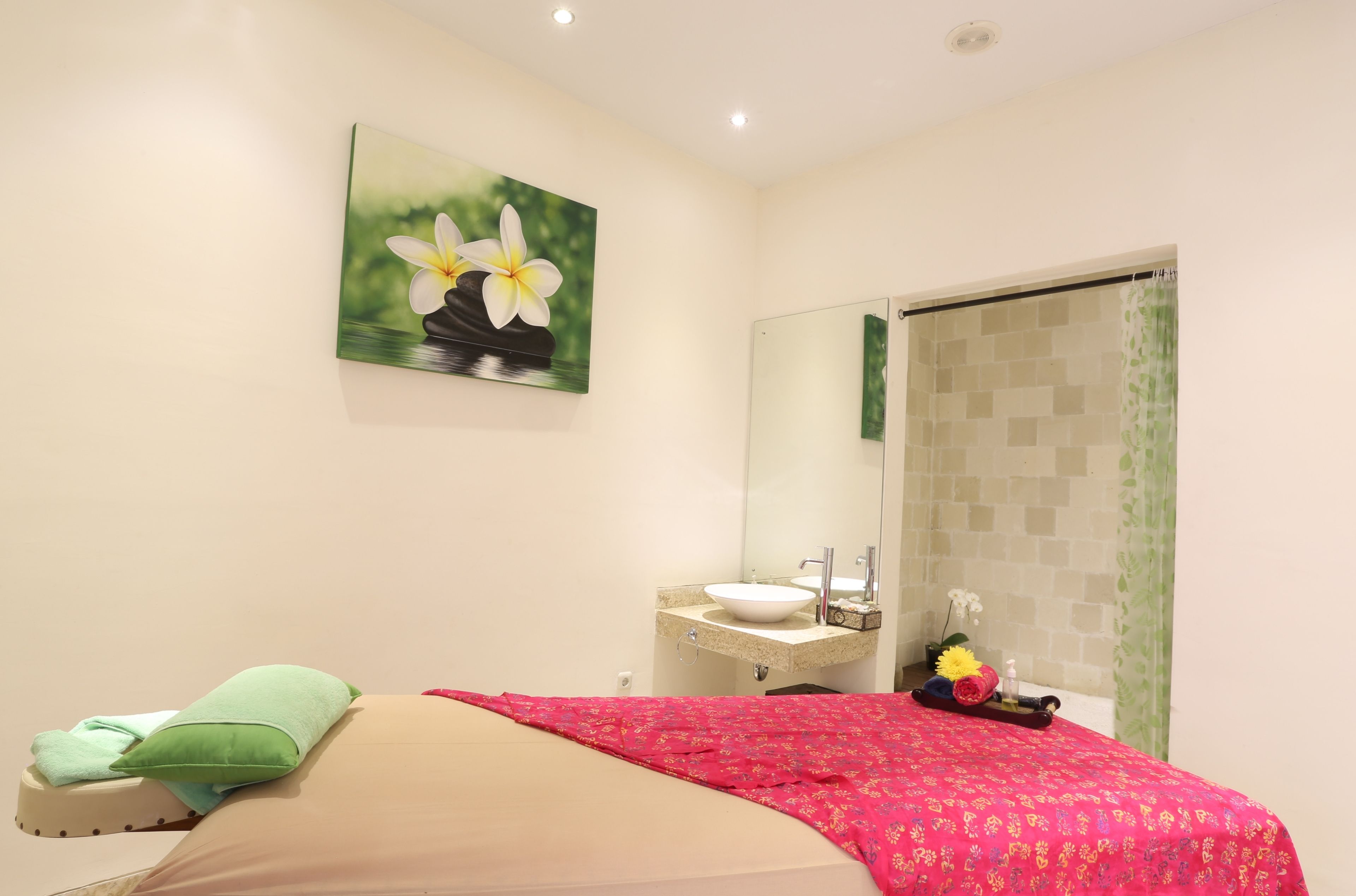 A bedroom with a bed, a bedside table, a mirror, a sink, and a shower area.