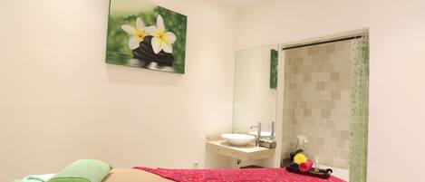 A bedroom with a bed, a bedside table, a mirror, a sink, and a shower area.