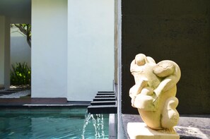 A stone sculpture by a pool with a water feature. - Jas Green Villas (Seminyak)