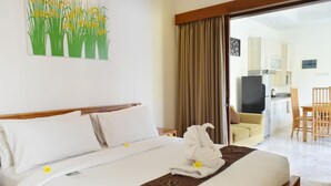 Habitación de hotel con una cama bien hecha, un comedor y una cocina visible a través de una puerta abierta.