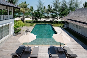 A pool area with lounge chairs and umbrellas, surrounded by a wooden deck and palm trees. - The Sanchaya (Bintan)