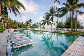 A poolside area with lounge chairs and palm trees. - The Sanchaya (Bintan)
