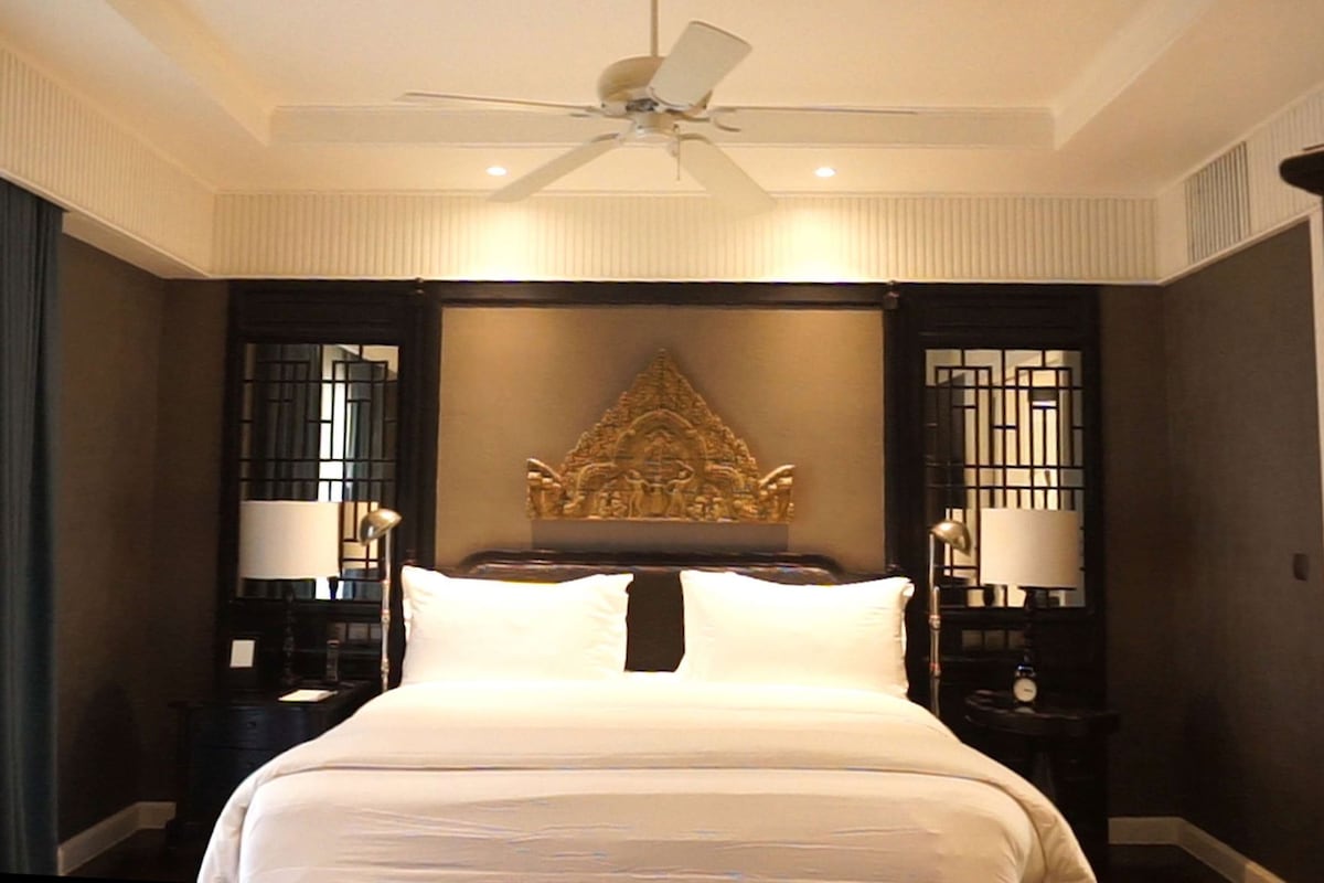 Una habitación de hotel con una cama grande, un ventilador de techo y un cabecero decorativo.