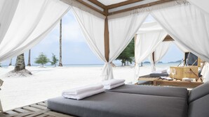 Une tente de plage avec un lit, un plateau contenant une bouteille, des verres et un livre.