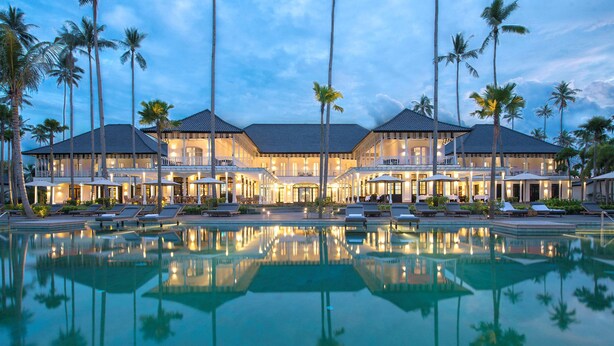 Un grand complexe hôtelier doté d’une piscine, de nombreuses chambres et de palmiers.