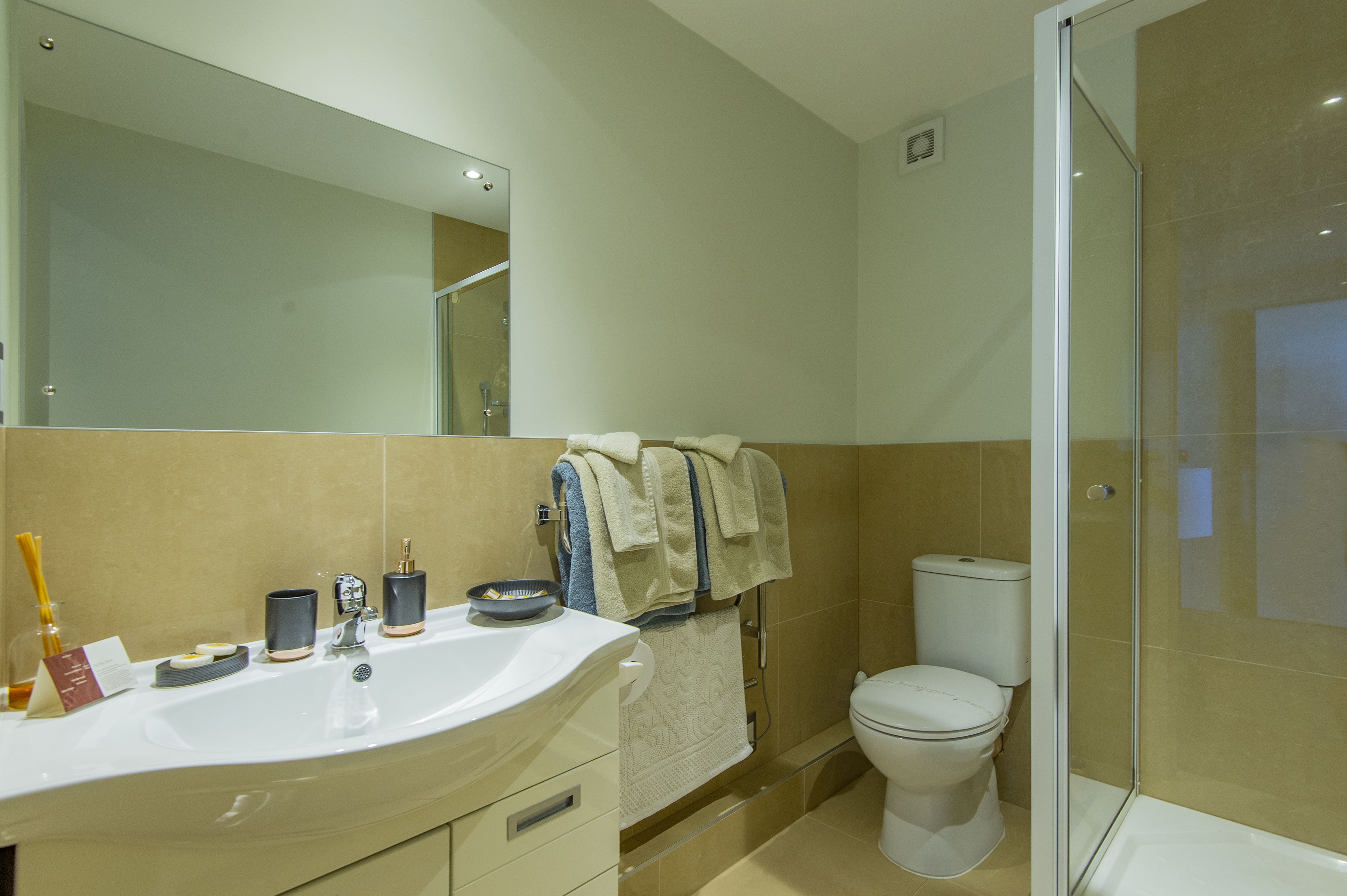 Un baño moderno con un espejo grande, un lavamanos con artículos de tocador, un inodoro y una ducha con cerramiento de vidrio.
