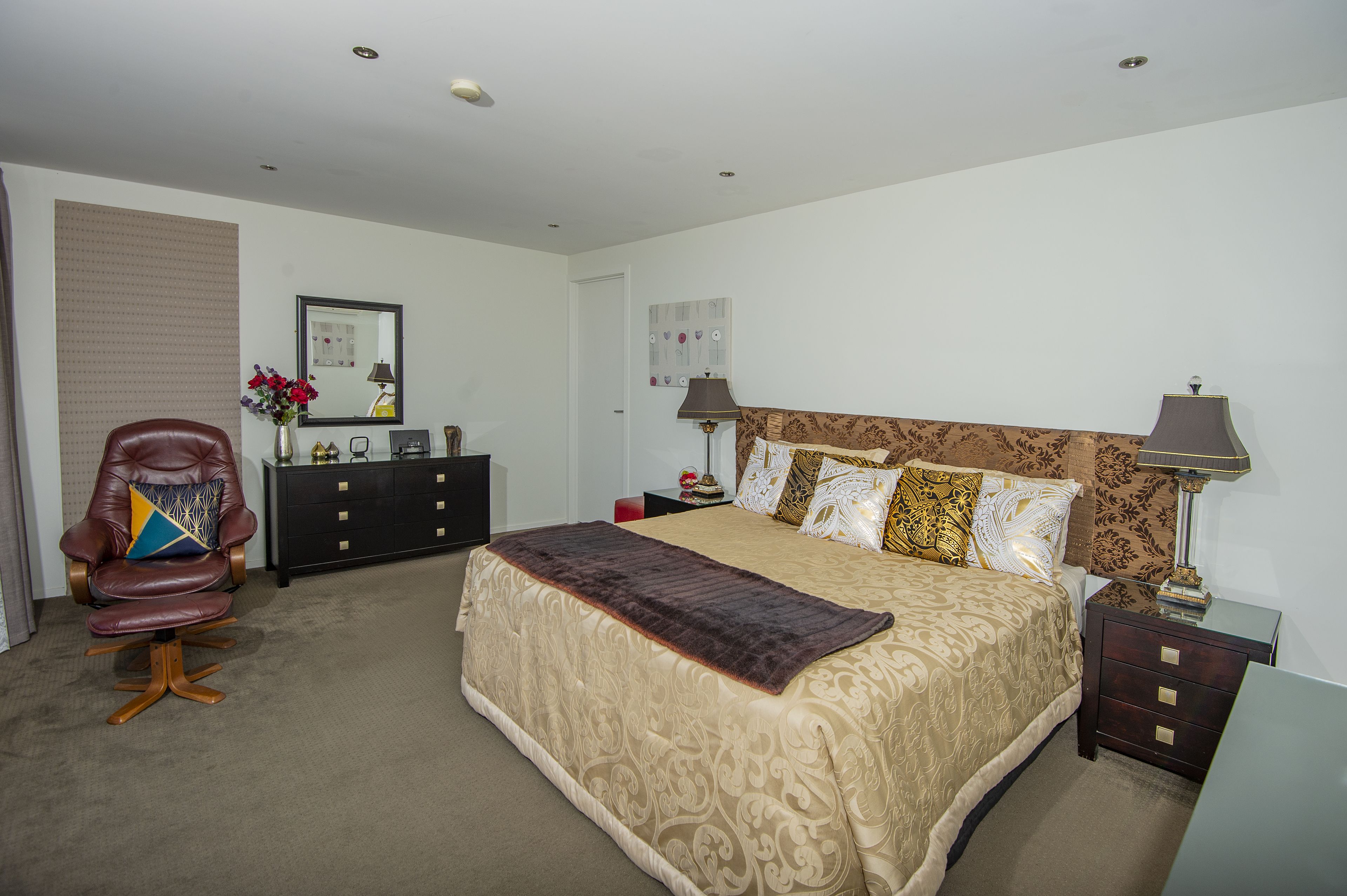 A bedroom with a large bed, a leather armchair, a dresser, and two bedside lamps.
