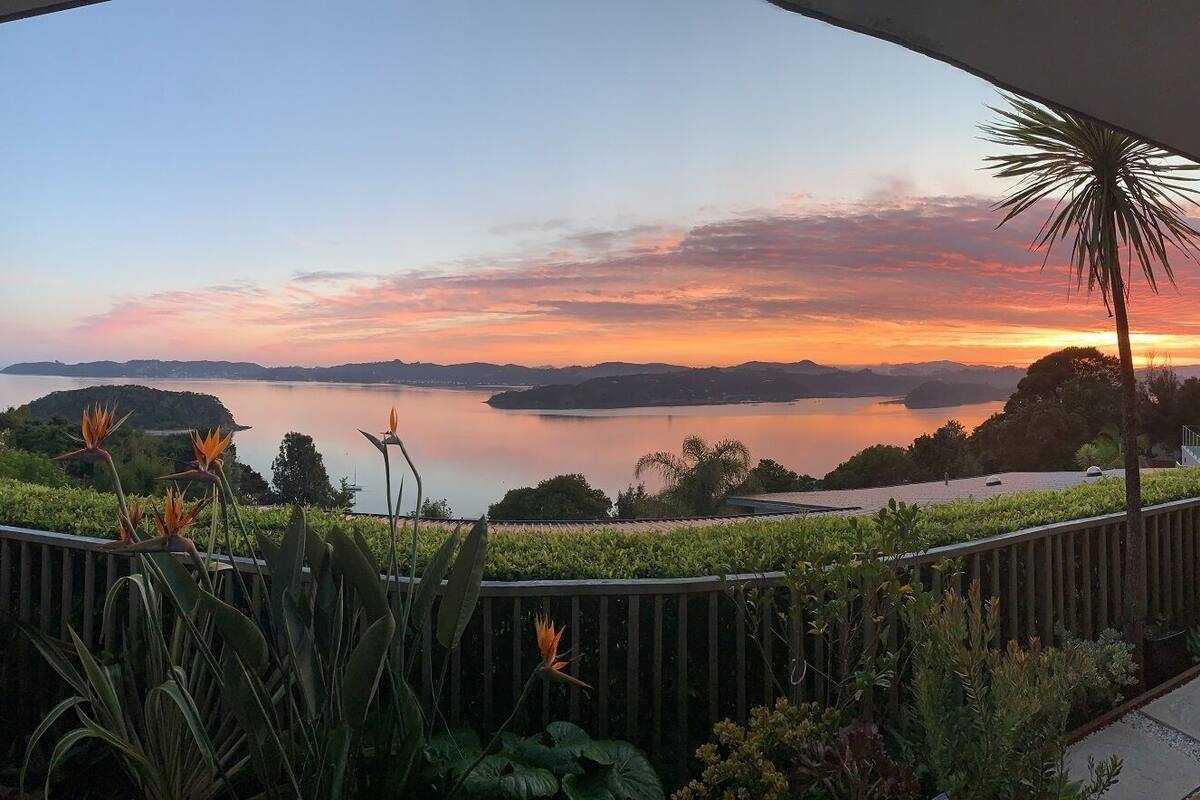 Un balcón con vistas a una puesta de sol sobre aguas tropicales, rodeado de follaje exótico.