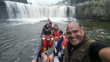 A group of people in a boat on a river with a waterfall in the background.