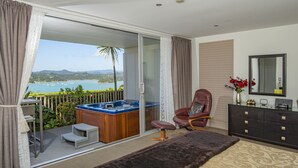 A bedroom with a large bed, a chair, a hot tub, and a view of the sea. - Tarltons Lodge (Paihia)