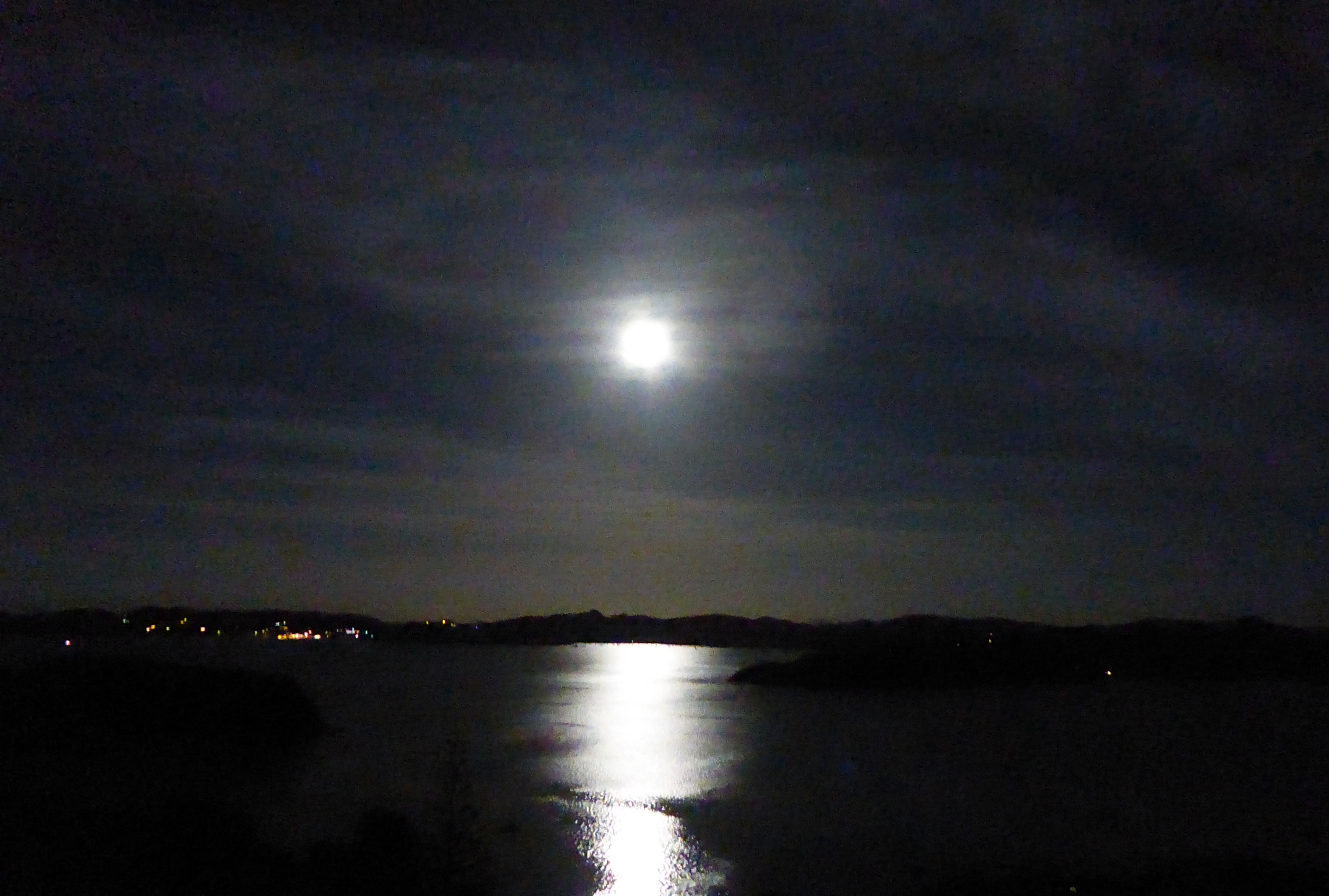 Une scène nocturne avec une lune brillante se reflétant sur une étendue d’eau.