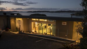 A modern building with a glass entrance, a parking area, and a view of the sea and hills. - Tarltons Lodge (Paihia)