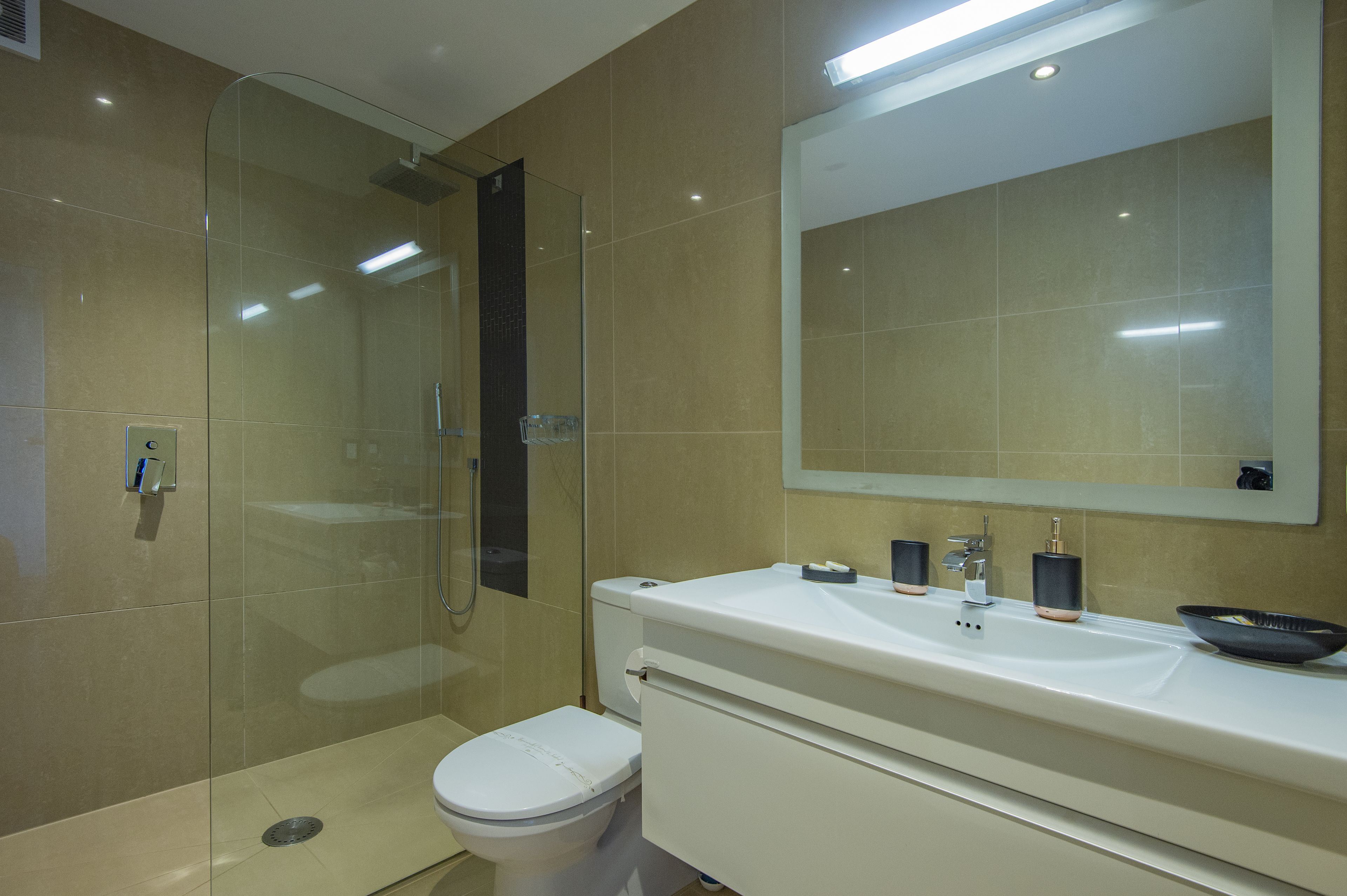 A modern bathroom with a glass shower enclosure, a white toilet, and a large mirror above a white sink with a bowl.