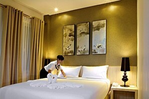 A hotel room with a neatly made bed, a nightstand with a lamp, and three framed artworks on the wall. - HW Hotel Padang (Padang)