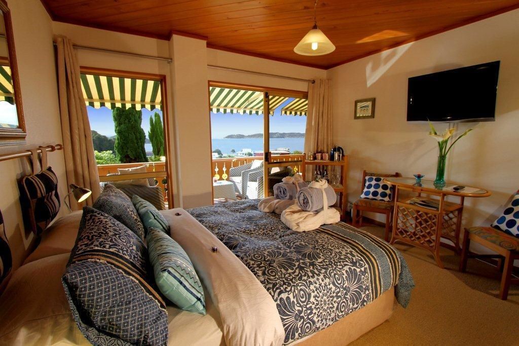 A bedroom with a large bed, a TV, a small table with a vase, and a view of the sea.