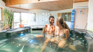 A couple in a hot tub with a wooden ceiling and tiled walls. - Chalet Romantica (Paihia)