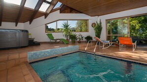 An indoor swimming pool with a wooden ceiling, large windows, and lounge chairs. - Chalet Romantica (Paihia)