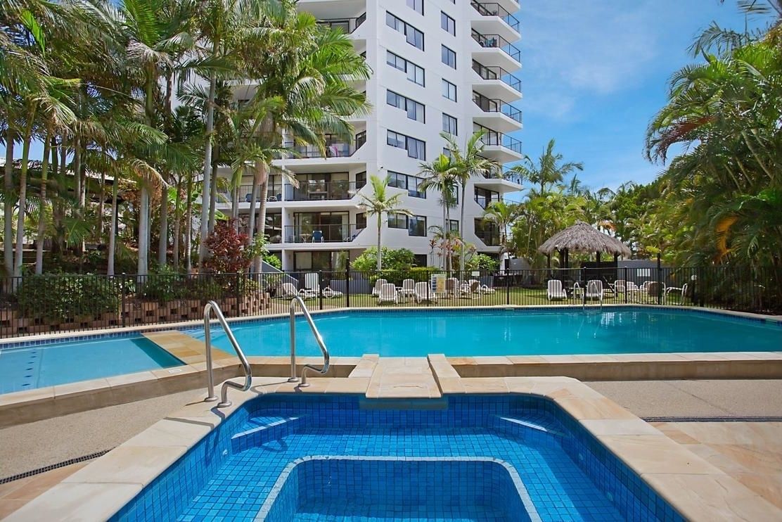 A swimming pool surrounded by palm trees and a multi-story hotel building.