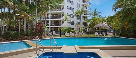A swimming pool surrounded by palm trees and a multi-story hotel building.